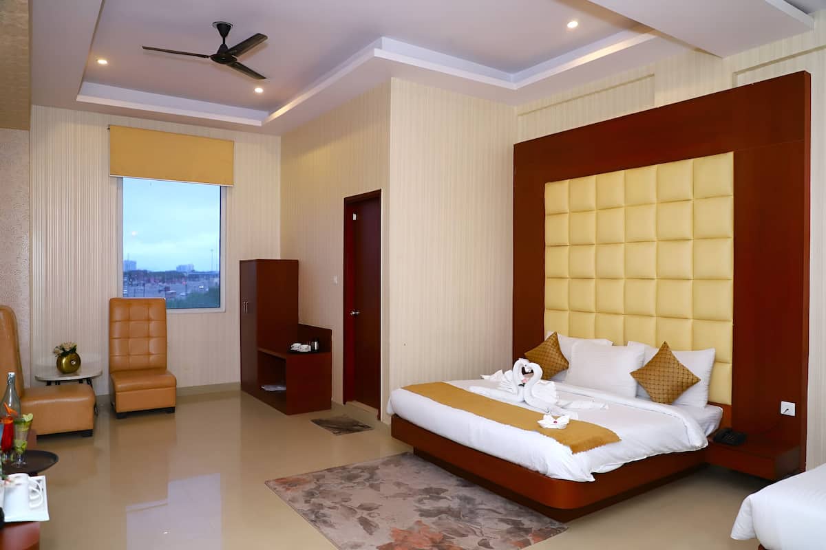 A modern hotel room with a large bed, a seating area with a chair and table, a small table with a bottle and glasses, and a window with a city view.