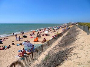 Une plage où des gens se prélassent au soleil et se baignent, une clôture en bois et un ciel dégagé.