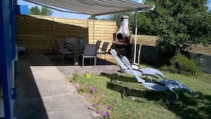 A backyard with a wooden fence, a barbecue grill, a table with chairs, and a garden area with flowers.