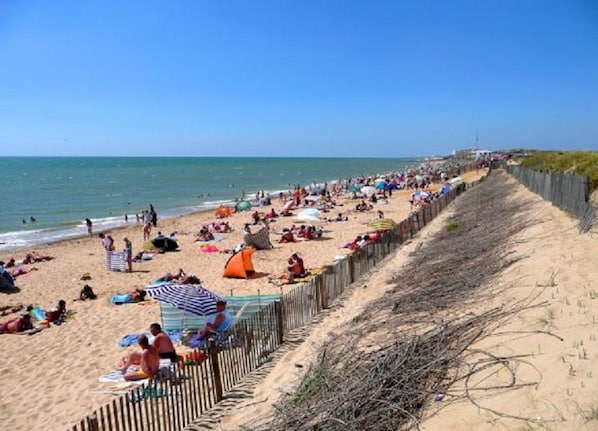 A beach with people sunbathing and swimming, a wooden fence, and a clear sky.