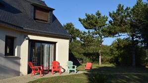 Une maison avec un toit en pente, une porte-fenêtre coulissante et un petit patio agrémenté de quatre fauteuils Adirondack de couleur rouge, verte et bleue.
