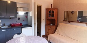 Quarto compacto com cozinha compacta, um armário de madeira, um sofá e um espelho.