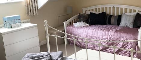 Un dormitorio con una estructura de cama metálica blanca, una colcha acolchada rosa y un aparador blanco con una caja azul encima.