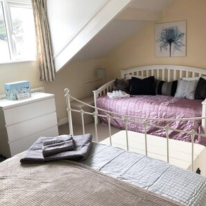A bedroom with a white metal bed frame, a pink quilted bedspread, and a white dresser with a blue box on top. - Brackencrag (Windermere)