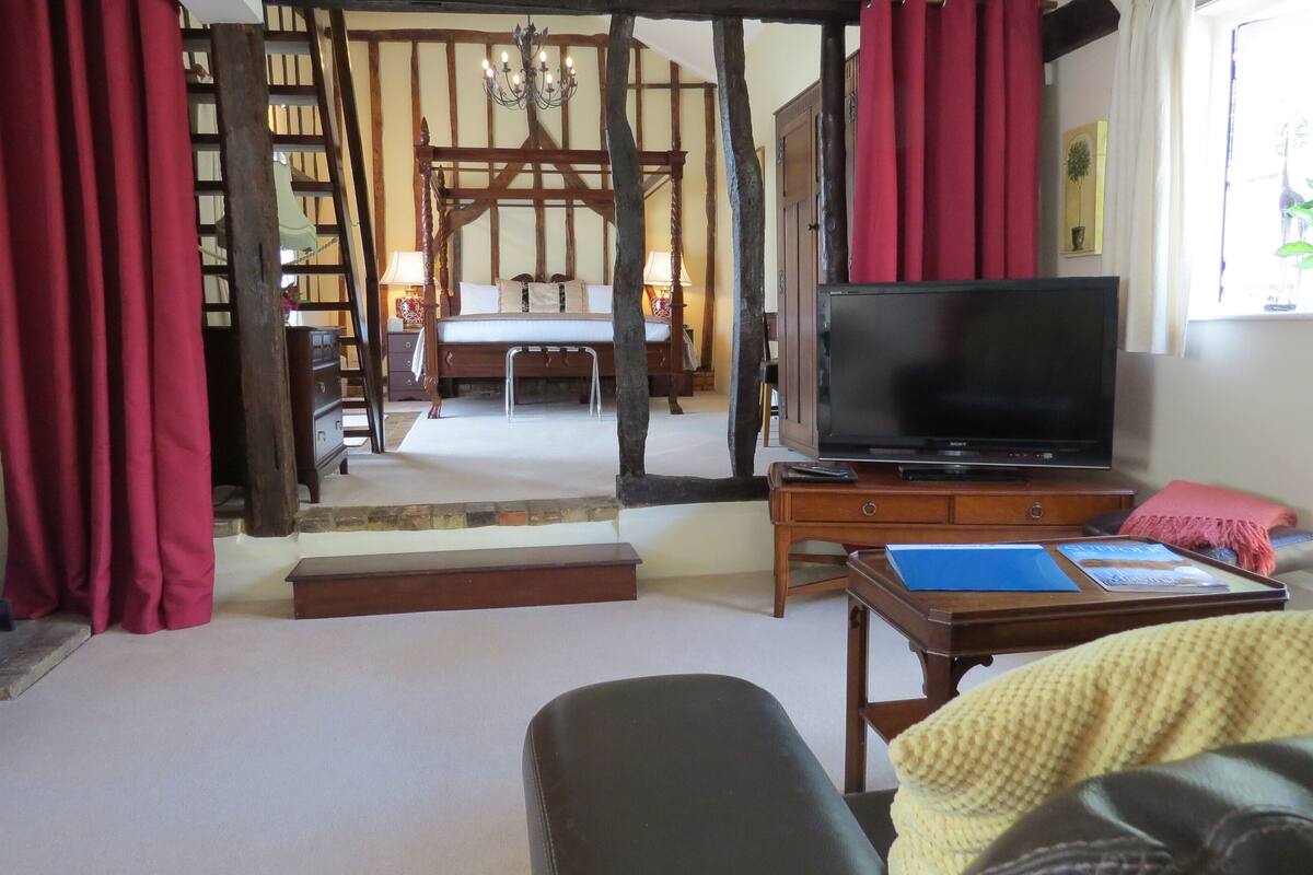 A room with a bed, a television, a wooden desk, and a red curtain.