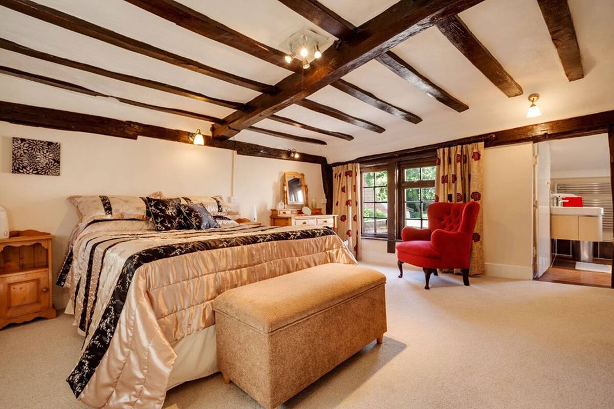 A bedroom with a large bed, a red armchair, and a wooden ceiling.