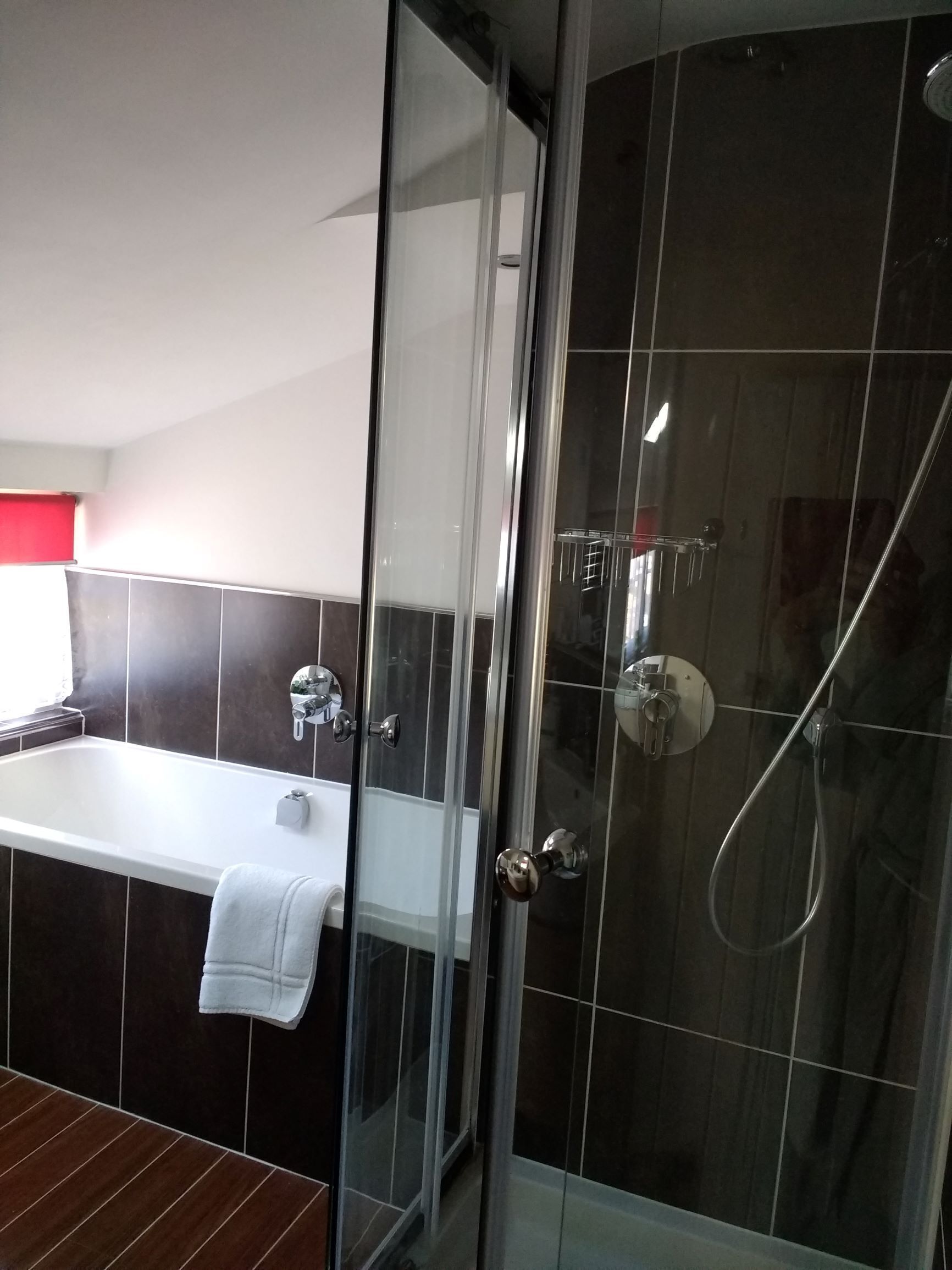 A modern bathroom with a glass-enclosed shower, a white bathtub, and dark tiled walls.