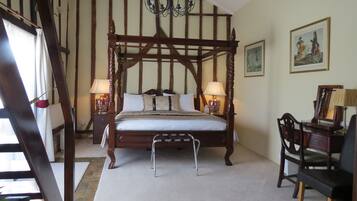 A traditional four-poster bed with a canopy, two bedside tables with lamps, a wooden chair, and a framed painting on the wall.