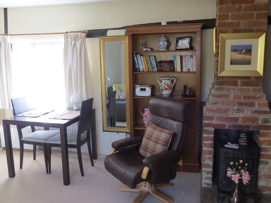 A living room with a fireplace, a bookshelf, a dining area with a table and chairs, and a large mirror.