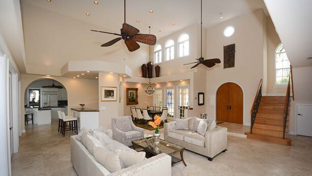 A spacious living room with a high ceiling, two ceiling fans, a dining area, and a staircase leading to an upper level. - Las Olas Waterfront Mansion (fort lauderdale)