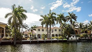 A waterfront property with a row of buildings, palm trees, and a dock with a boat. - Las Olas Waterfront Mansion (fort lauderdale)