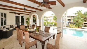 A dining area with a wooden table and wicker chairs, a ceiling fan, and a view of a swimming pool. - Las Olas Waterfront Mansion (fort lauderdale)