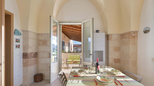 A dining area with a table set for four, a bottle of wine, and a view of the outside.