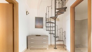 A room with a spiral staircase, a wooden door, a beige dresser, and a framed picture on the wall.