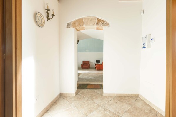 A hallway with a tiled floor, a decorative archway, and a seating area with a chair and a table in the background.