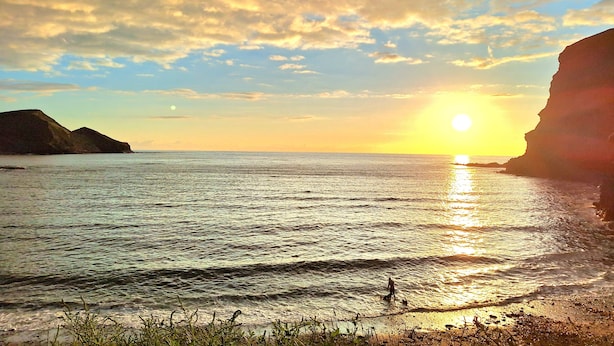 Un atardecer sobre un mar tranquilo con acantilados a ambos lados.