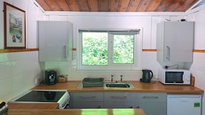Una cocina con armarios blancos, un ventanal con vistas a zonas verdes, microondas, cafetera y lavavajillas.
