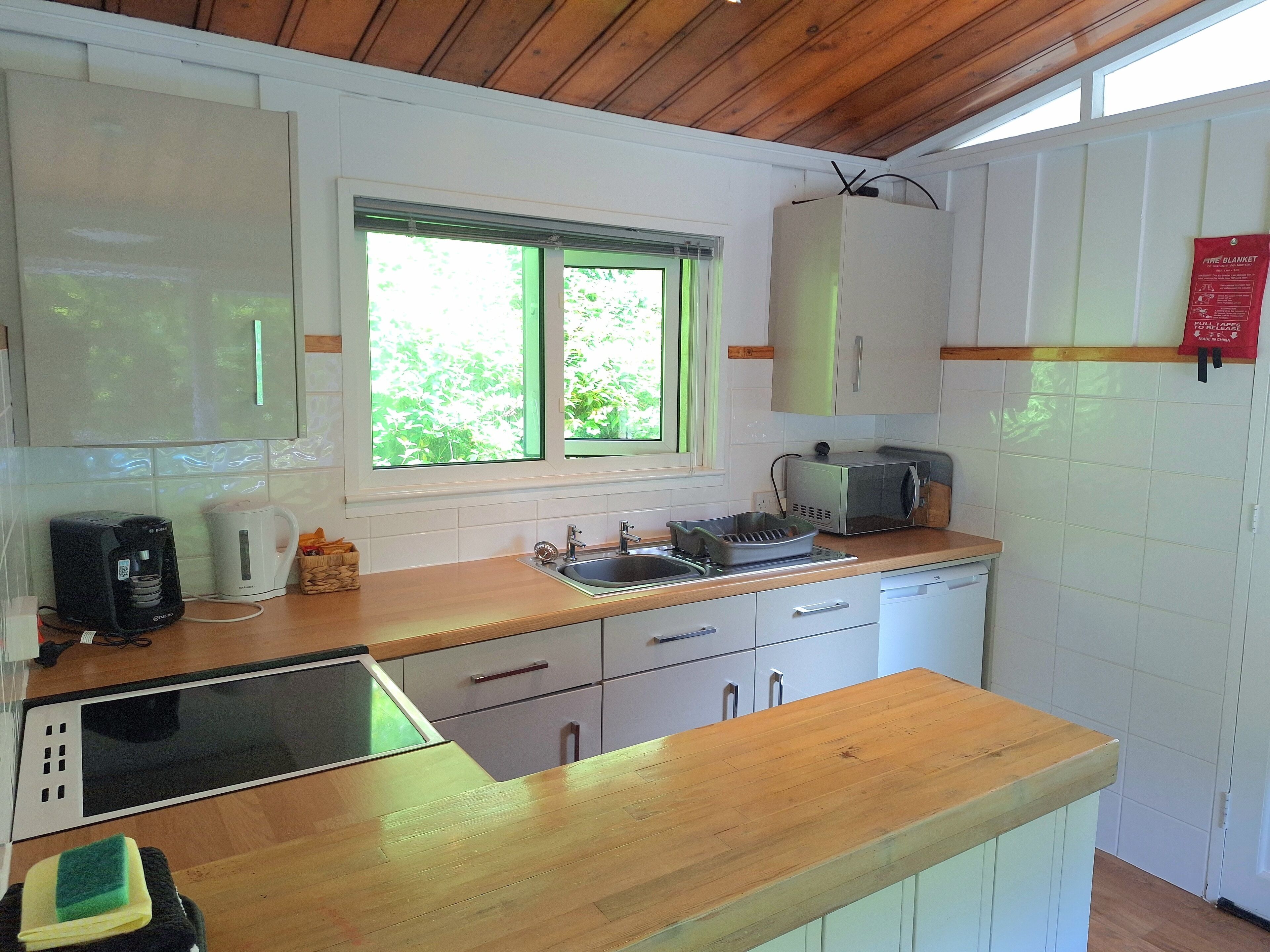 A kitchen with white cabinets, a wooden countertop, a microwave, a toaster, and a window with green blinds.