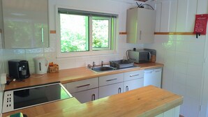 A kitchen with white cabinets, a wooden countertop, a microwave, a toaster, and a window with green blinds. - Parada Cottage@Mineshop Holiday Cottages, a woodland stroll to Crackington Haven (Bude)