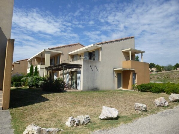 A modern residential building with a flat roof, a covered entrance, and a well-maintained lawn with large rocks.