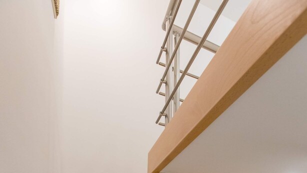 A wooden staircase with a glass railing leading to a white closet with shelves. - Apartment Dam (Dubrovnik)