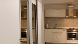 A modern kitchen with white cabinets, a stainless steel oven, and a sliding glass door leading to another room. - Apartment Dam (Dubrovnik)