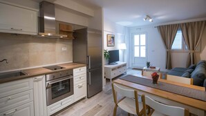 A modern kitchen with stainless steel appliances, a dining area with a wooden table and chairs, and a living room with a sofa and a TV. - Apartment Dam (Dubrovnik)