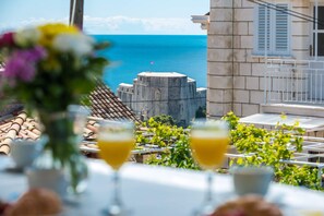 A table with drinks and a view of a coastal area with a building and the sea. - Apartment Jele (Dubrovnik)