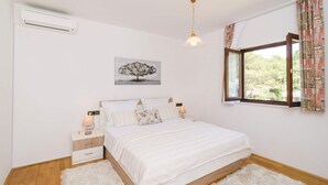Un dormitorio con cama, mesita de noche, lámpara, ventana con cortinas y aire acondicionado de pared.