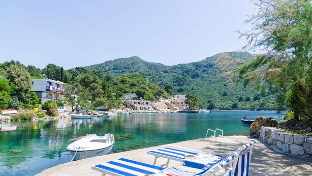 Zona ribereña con sillones de descanso, un muelle con un bote y edificios al fondo.