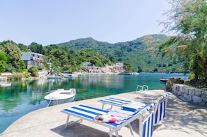Zona ribereña con sillones de descanso, un muelle con un bote y edificios al fondo.