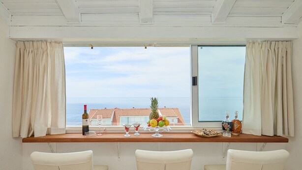 Un balcon avec une table en bois, trois chaises blanches et une vue sur la mer.
