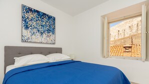 A bedroom with a bed, a window with a view of a building, and a painting on the wall. - Dominium Old City Suite (Dubrovnik)