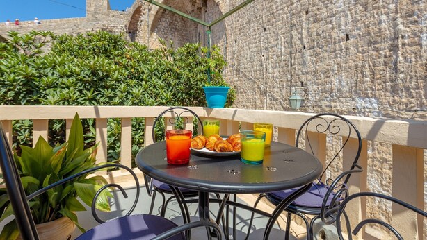 A round table with chairs on a balcony, a plate of croissants, and two glasses of orange juice. - Dominium Old City Suite (Dubrovnik)
