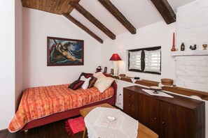 A cozy bedroom with a bed, a wooden dresser, a nightstand, a red lamp, and a painting on the wall. - Gina Apartment (Dubrovnik)