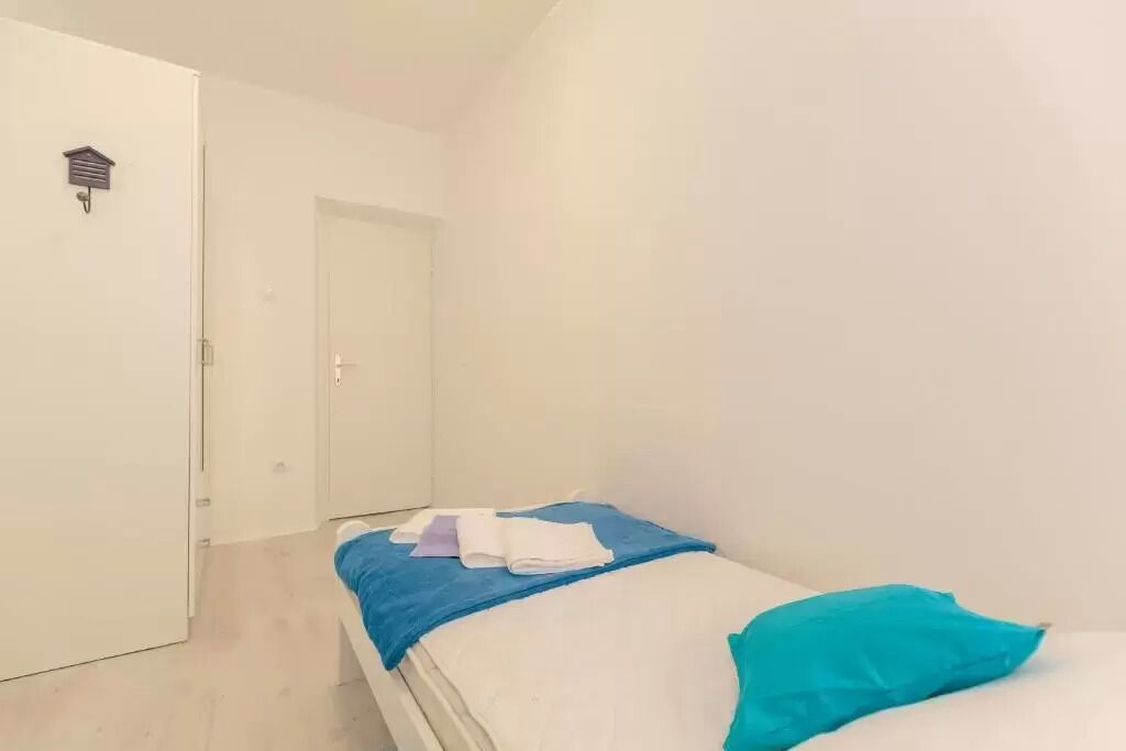 A small, clean room with a bed, a door, and a wall-mounted light fixture.