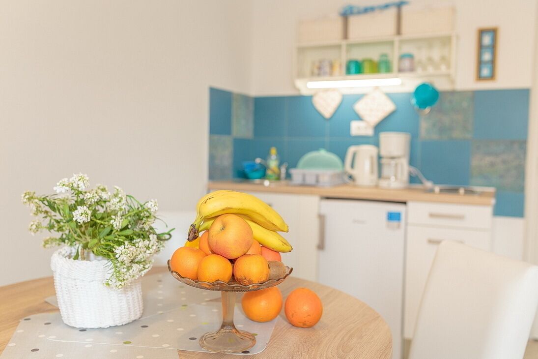 A kitchen with a fruit bowl on a table, a potted plant, and a coffee maker.
