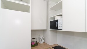 A modern kitchen with white cabinets, a microwave, a kettle, and a small countertop.