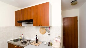 A kitchen with wooden cabinets, a stainless steel sink, a wooden cutting board, and a wine bottle. - Studios Lončarica (Dubrovnik)