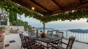 Eine Terrasse im Freien mit Tisch und Stühlen, einem Steinkamin und Meerblick.
