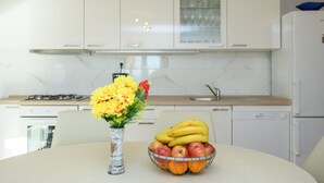 Eine Küche mit weißen Schränken, einem Herd und einem Spülbecken. Auf der Arbeitsfläche steht eine Vase mit Blumen und eine Schüssel mit Obst.
