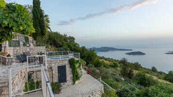 A stone building with a balcony overlooking a body of water and hills.