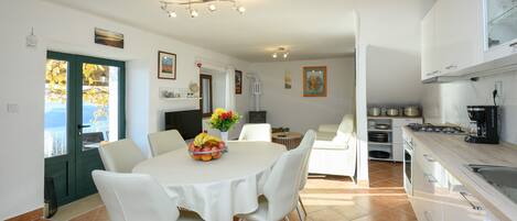 A modern kitchen with white cabinets, a dining area with a round table and white chairs, and a view through a green door.