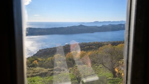 Blick aus einem Fenster auf eine Küstenlandschaft mit Hügeln und einem Gewässer.