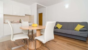 A modern kitchen with white cabinets, a round dining table with two chairs, and a grey sofa with yellow cushions. - Vintage Dream Peyton Apartment (Dubrovnik)