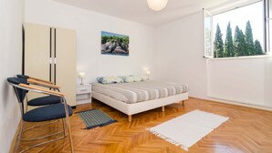 A bedroom with a bed, a desk with a chair, a wardrobe, a nightstand, a lamp, a window with a view of trees, and a picture on the wall. - Vintage Dream Peyton Apartment (Dubrovnik)