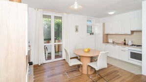 A modern kitchen with white cabinets, a round wooden table, and a hanging light fixture. - Vintage Dream Peyton Apartment (Dubrovnik)
