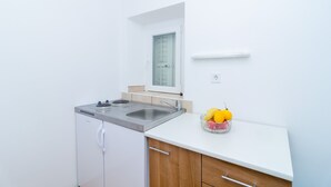 Une cuisine compacte équipée d’un lave-vaisselle intégré, d’un évier et d’un petit plan de travail sur lequel se trouve un saladier rempli de fruits.