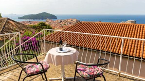 Un balcon avec une table et des chaises, donnant sur une ville côtière et la mer.