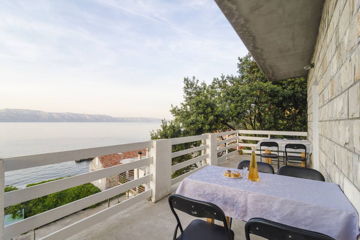 A terrace with a table set for two, overlooking a body of water and distant mountains.